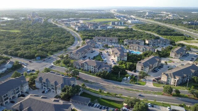 Winding arterial road passes apts in Westover Hills area toward distant roller coaster tracks. High angle perspective details regional transportation routes across Bexar County, San Antonio, TX