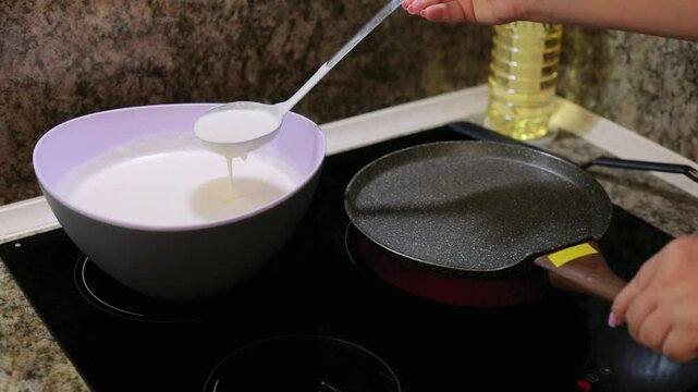 Pouring batter onto a hot pan on the stove to fry pancakes for Maslenitsa, a traditional cooking process for a festive homemade breakfast