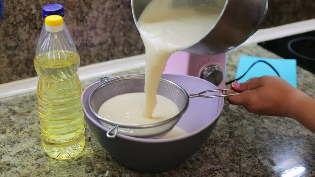 Straining smooth pancake batter through a sieve into a bowl to remove lumps, an essential step in preparing homemade dough for baking