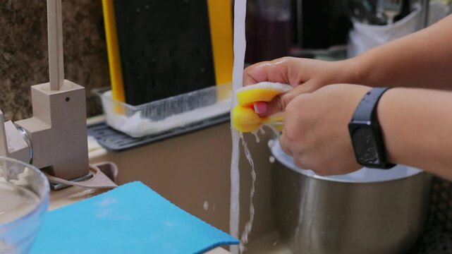 Washing dishes under running water in the kitchen sink with a soapy sponge, a simple everyday cleaning routine at home