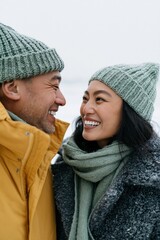 Fototapeta premium Smiling winter couple portrait in knitted hats and scarves for cozy holiday banner and seasonal background