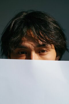 Half face portrait of young man peeking over white paper sheet for minimal portrait background or banner