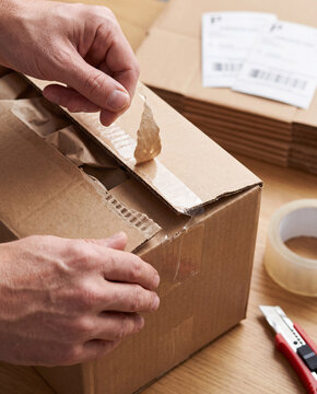 Hands tear open the taped flap of a corrugated shipping box