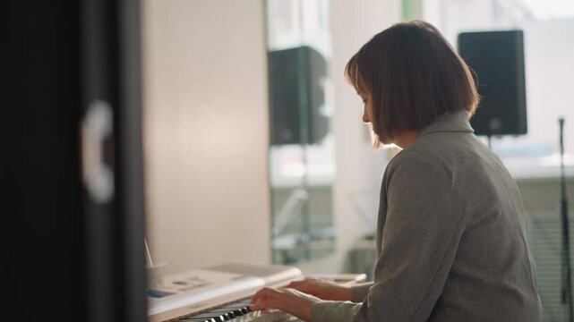 Sunlit studio keyboard session white female songwriter composing melody with introspective posture, soft backlight, speaker and laptop nearby, intimate creative mood, demo recording vibe, reflective