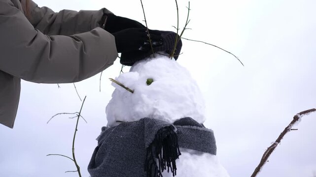 A person puts a warm knitted scarf around a snowman outdoors in fresh winter snow. Cozy scene evoking winter fun, Christmas holidays