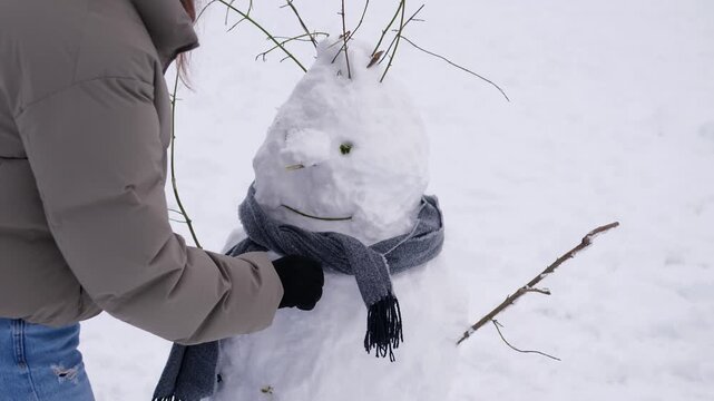 A person puts a warm knitted scarf around a snowman outdoors in fresh winter snow. Cozy scene evoking winter fun, Christmas holidays