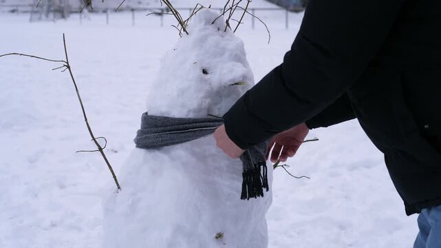 A person puts a warm knitted scarf around a snowman outdoors in fresh winter snow. Cozy scene evoking winter fun, Christmas holidays