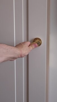 Man's hand reaching for and turning a golden handle to open a white interior door, revealing a modern kitchen and dining area before closing the door again, symbolizing opportunity and passage