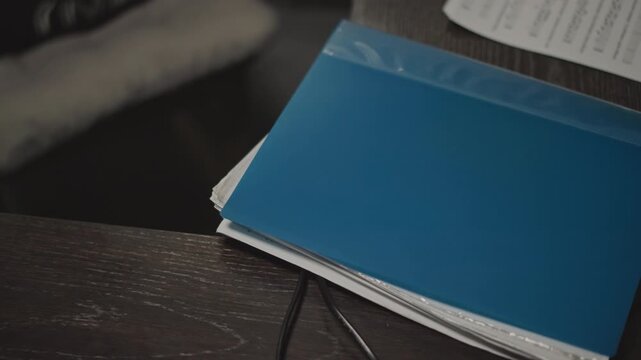 Blue music notebook lies on desk with sheet music peeking from pages, coiled cable resting beside spiral binding, dark wood surface and soft lowkey lighting create intimate studio atmosphere, music