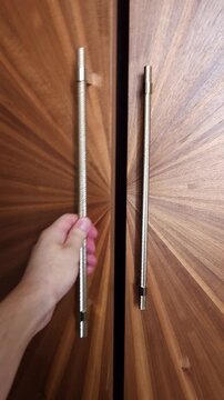 Person opening a stylish modern wardrobe door with a distinctive sunburst wood grain pattern, revealing the dark interior of the elegant custom made furniture and its minimalist metal handle