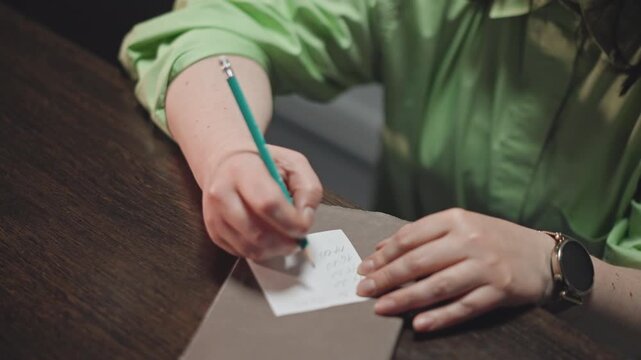Caucasian educator writing musical notes carefully. Music instructor jotting down notes at wooden desk. Teacher wearing green shirt focusing on composing melody and planning lessons diligently