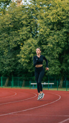 Obraz premium Young woman running on a red track with green trees in the background