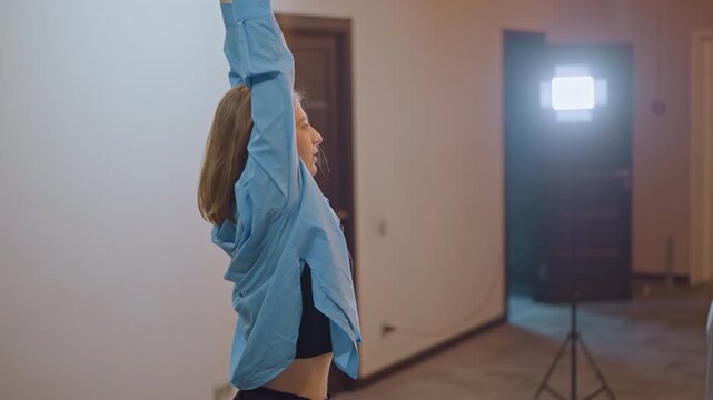 Artist in studio extends arms high. Ballet dancer stretching upward with extended limbs in studio. Professional performer in studio assumes elevated stance with outstretched arms during rehearsal