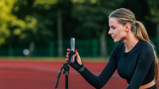 Young woman athlete recording workout video on smartphone at outdoor track