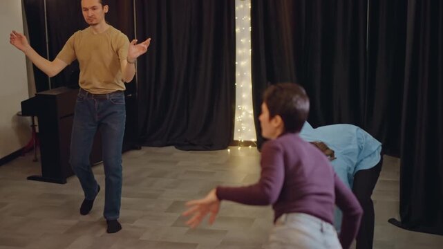 White ensemble doing energetic group warmup, actors and dancers play with improv and timing, coach leads movement across studio floor, curtain and fairy lights, chairs stacked to side, laughter