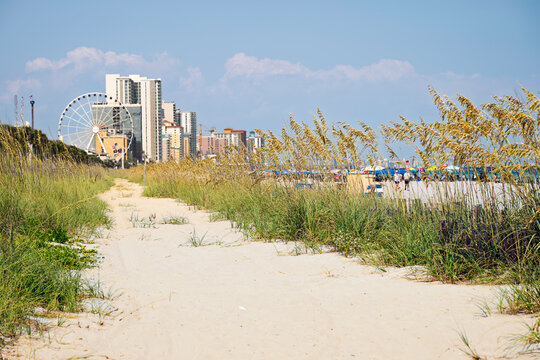The downtown Boardwalk and promenade of resorts and attractions shimmers under summer heat haze from atmospheric distortion along a sandy beach in Myrtle Beach, South Carolina.