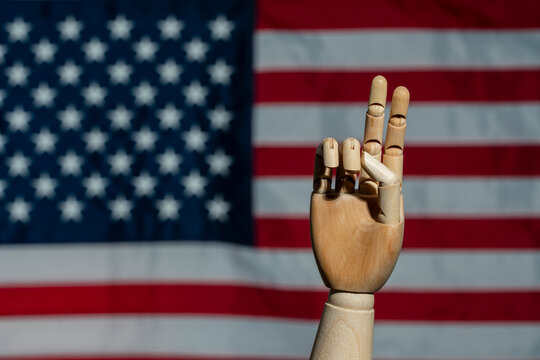 US election victory gesture with wooden hand and flag. Wooden mannequin hand showing the peace or victory V sign on blurred American flag background symbolizing US election success and democracy