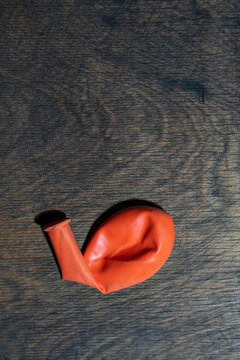 Deflated orange balloon on dark wooden background, closeup. Single flat deflated orange rubber balloon lying on textured dark wood surface with copy space representing end of party or disappointment
