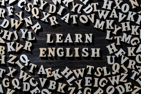Learn English concept with wooden letters background. Words Learn English formed with wooden letters surrounded by jumble of alphabet characters on dark background representing language education