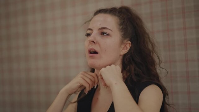 Vocal coach practicing breath warmups indoors classroom, hands near throat, expressive face, plaid wallpaper background, private lesson mood with focused technique and gentle guidance