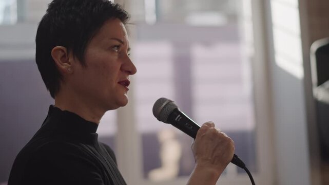 Student and coach trading microphone during lesson, coach demonstrating breathing and tone, mentor providing feedback and guidance, intimate classroom studio setting, focus on technique and harmony