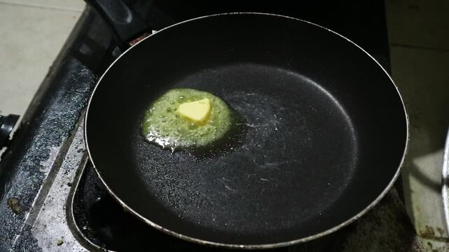 A small piece of yellow butter melting in a hot black frying oiled pan. 