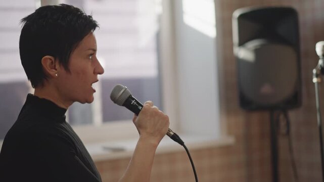 Performer practicing with sound equipment. Artist rehearsing alongside audio monitors in sunlight. Performer adjusts microphone and monitors as sunlight filters through window in rehearsal setting