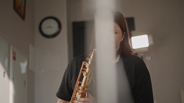 Student practicing saxophone in school corridor under hallway lights and clock, audition rehearsal with coach off camera, expressive dynamics and concentrated breath control, camera recording