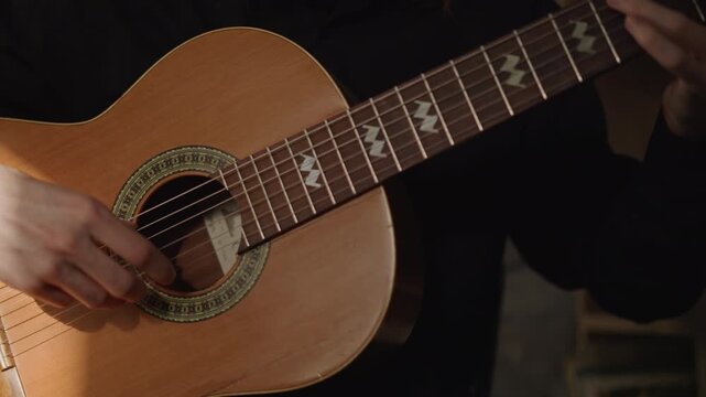 Closeup hands on acoustic guitar practicing chord transitions in dim studio light, musician tutor coaching fingerstyle technique with nylon strings and worn wood, bracelet on wrist, focused mood