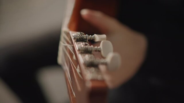 Hands adjust tuning pegs carefully. Focus on precise adjustment of guitar tuning pegs during practice. Calmly tuning guitar strings with careful attention to hardware for optimal sound quality