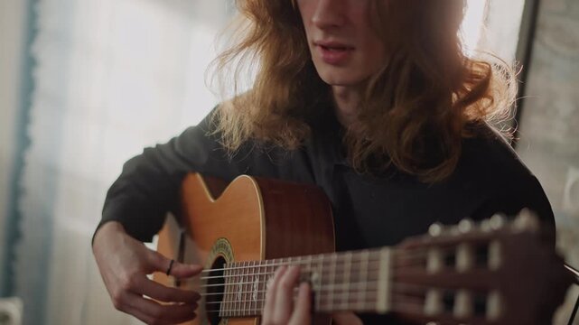 Sunlit young musician playing acoustic guitar, coachstyle lesson vibe in home studio, long hair profile with warm backlight, fingerpicking and strumming, expressive portrait and candid rehearsal