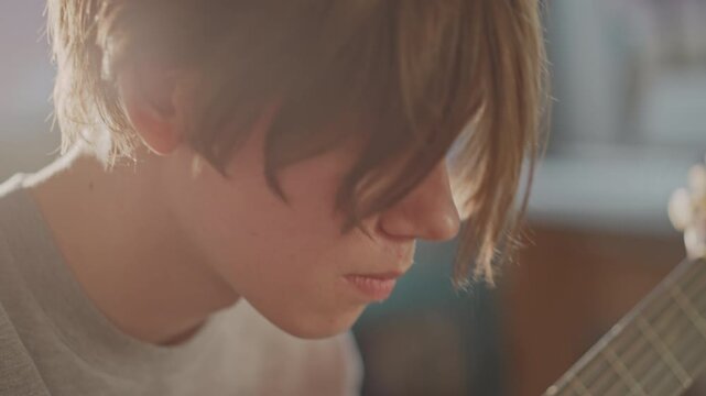 Teen practicing mellow acoustic guitar. Student concentrating on fingerstyle guitar in classroom. Peaceful environment where teenager refines fingerpicking techniques during warm classroom session