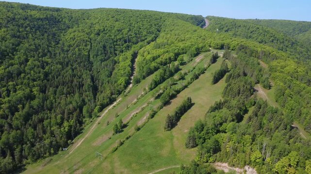 Aerial drone footage shows the green summer ski slopes of Le Petit Chamonix in Matapedia, Quebec, surrounded by dense Appalachian forest and rolling mountain terrain.