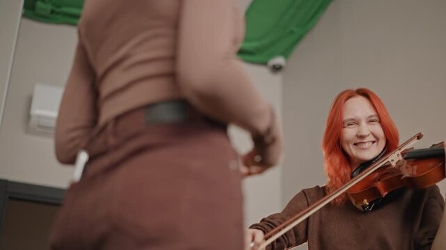 Enthusiastic teacher guides young violinist. Bright studio environment with encouraging violin lessons. Cheerful instructor assists student in mastering bowing techniques effectively
