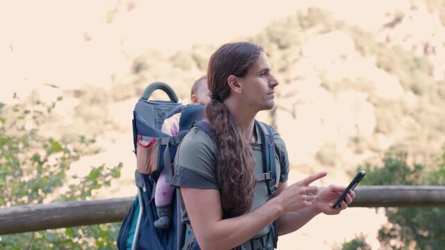 Father with baby carrier using smartphone for hiking navigation