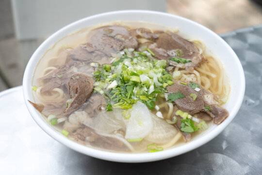 A bowl of traditional Lanzhou beef noodle soup featuring tender braised beef slices, clear savory broth, wheat noodles, daikon radish, scallions, and fresh cilantro.