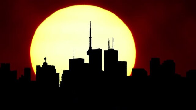 City skyline silhouette with hot cinematic sun set, downtown cityscape with large sun disk sunset light. Artistic effects shimmering air mist. Epic hot summer sky after rain. Heat wave alert warning.