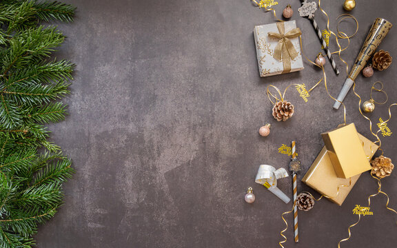 Overhead Christmas composition featuring wrapped gifts ribbons wooden ornaments dried botanical elements and evergreen branches arranged around a dark gray background