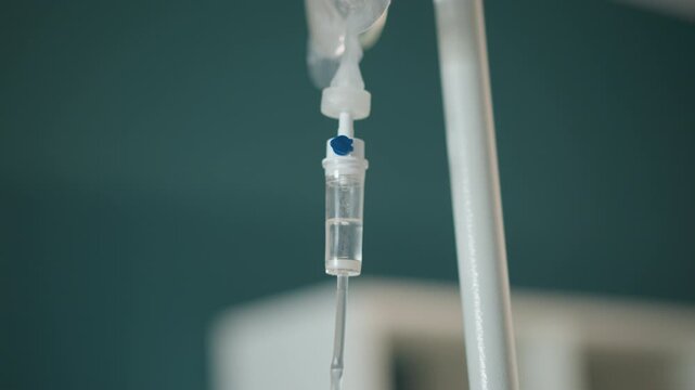 Iv drip hanging in ambulance interior paramedic secures tubing and clamp during emergency transport, closeup of drip chamber and saline flow, portable monitor and stretcher blurred in background,