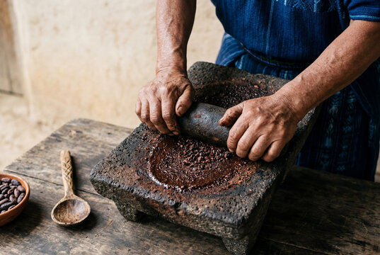 Hands grinding toasted cacao beans on traditional stone metate tool