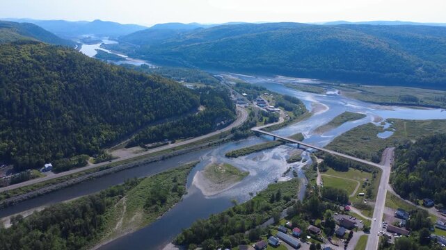 Aerial view of Matapedia, Quebec, showing winding river channels, a bridge, railway, roads and expansive forested Appalachian mountains.