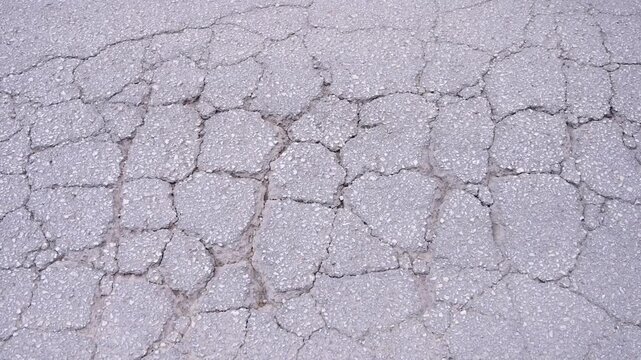 Cracking on asphalt surface. Crumbled street texture. Crocodile pattern road damage. Asphalt pavement deterioration. Damaged highway infrastructure.