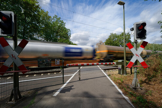 Closed level crossing with red St Andrews crosses. A freight train with tank cars passes the barrier with motion blur.