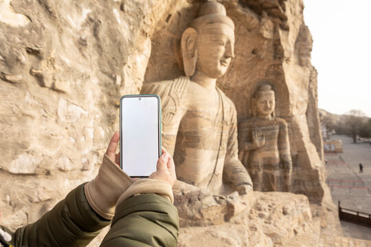 Person capturing Yungang Grottoes Buddha statue with smartphone