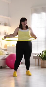Overweight woman exercising with hula hoop indoors. Sports equipment