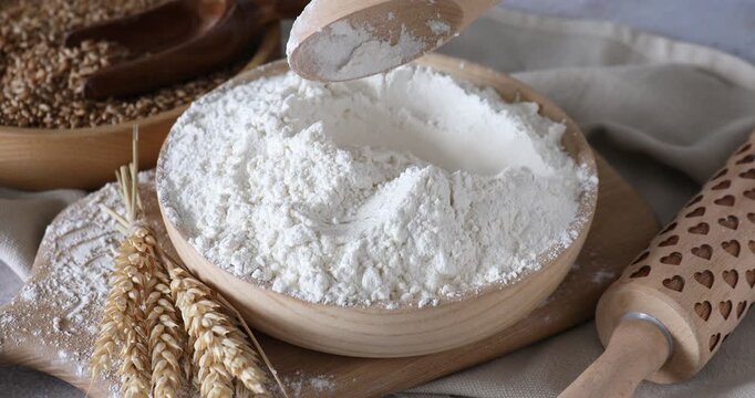 Woman taking wheat flour with spoon, spikes, grains and rolling pin at table, closeup