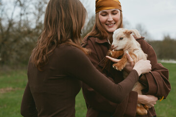 Obraz premium Goat kid with women outdoors, lifestyle, friendship, nature, countryside, warm scene of care and bonding in rustic setting, candid moment that conveys affection, calm mood, peaceful field