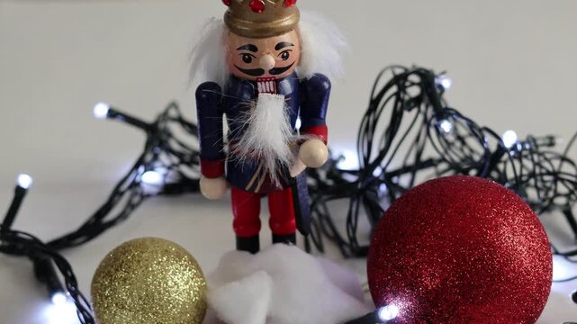 Una toma de cerca de un cascanueces o soldadito rodeado de bolas de navidad  con luz en un fondo blanco