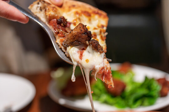 Hand holding spoon to lift stretchy cheese pizza slice