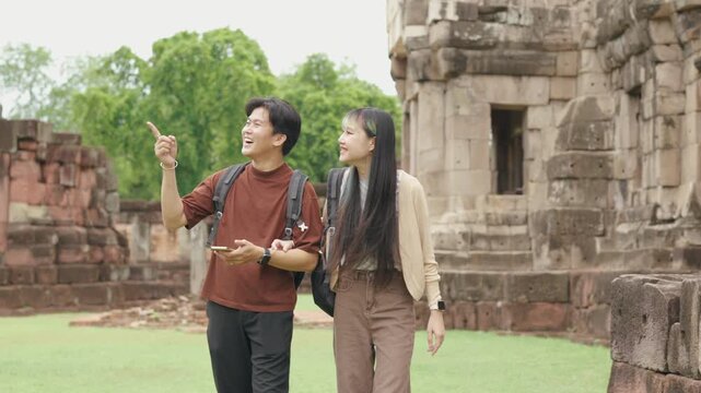 Attractive young Asian couple walking and exploring ancient historical temple ruins together. Cheerful romantic tourist lovers enjoying amazing cultural heritage during summer vacation.